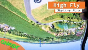 Blick aus der Onride-Perspektive der High Fly Attraktion im Skyline Park, während einer Überkopfdrehung mit einer grünen Landschaft und Parkstrukturen im Hintergrund.