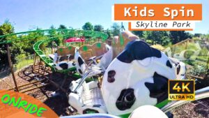 Onride-Perspektive der Kids Spin Achterbahn im Skyline Park, mit Kuhmuster-Wagen auf grünen Schienen in einer kindgerechten, bunten Umgebung.