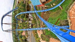 Onride-Perspektive der Achterbahn Fenix im Toverland mit blauen Schienen, steilen Kurven und einer thematisch gestalteten Umgebung aus grünen Pflanzen und Gewässern.