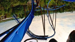 Onride-Perspektive der Achterbahn Fenix im Toverland, während einer Inversion auf blauen Schienen, umgeben von Bäumen und einer thematischen Landschaft.