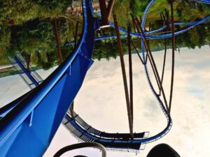 Onride-Perspektive der Achterbahn Fenix im Toverland, während einer Inversion auf blauen Schienen, umgeben von Bäumen und einer thematischen Landschaft.