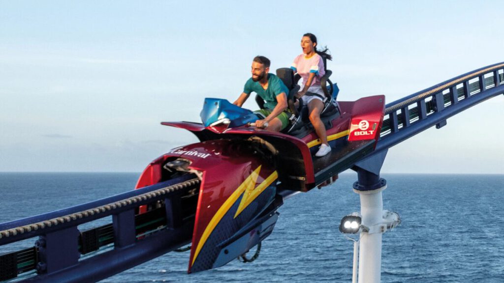 Zwei Personen fahren auf der Bolt-Achterbahn an Bord eines Kreuzfahrtschiffs mit Blick auf das offene Meer unter klarem Himmel.