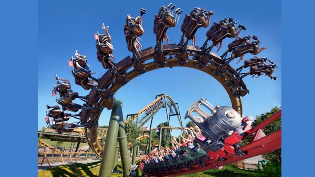 Ein Suspended Thrill Coaster von Vekoma, bei dem Fahrgäste kopfüber in einem Looping fahren. Die Wagen sind hängend befestigt, in einer thematisch gestalteten Bahn mit blauem Himmel.