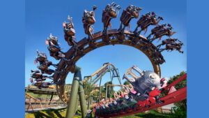 Ein Suspended Thrill Coaster von Vekoma, bei dem Fahrgäste kopfüber in einem Looping fahren. Die Wagen sind hängend befestigt, in einer thematisch gestalteten Bahn mit blauem Himmel.